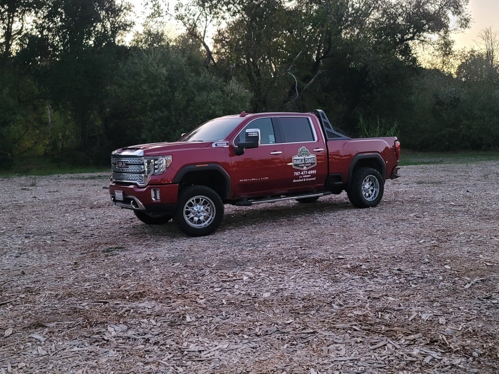 A red pickup truck, belonging to an emergency tree service, parked on a gravel area with trees in the background during dusk.